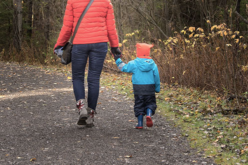 A woman holding a child's hand, walking along a path.