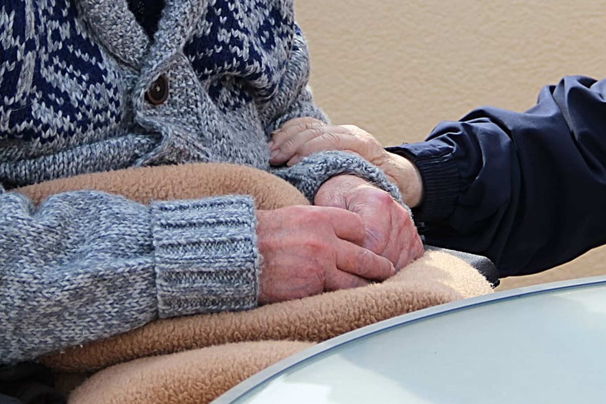 Elderly person's hands in lap with another's hand holding their arm caringly